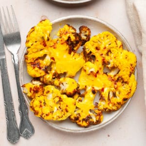 Cauliflower steaks in a plate with a fork and knife on the side.