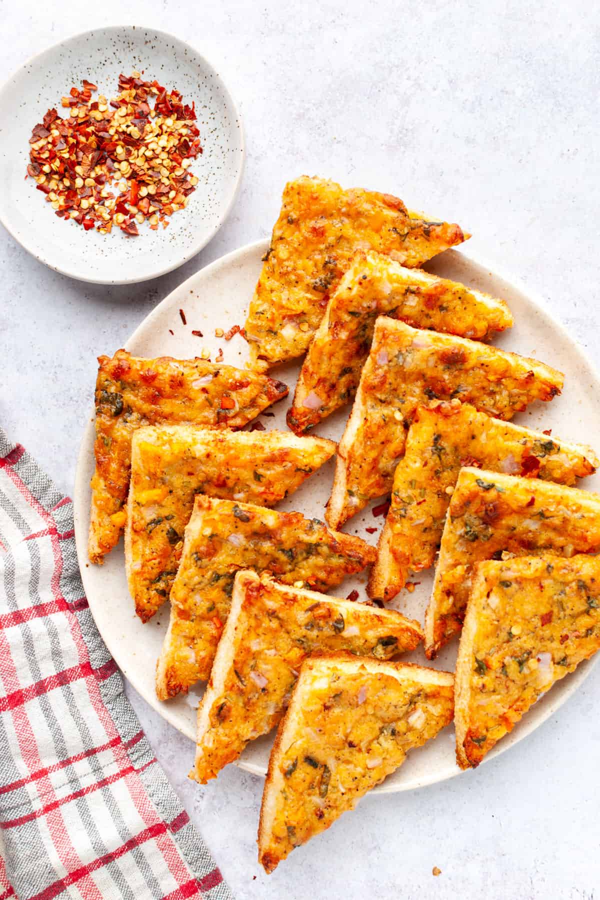 Chilli cheese toast triangles on a platter with chilli flakes on top left.