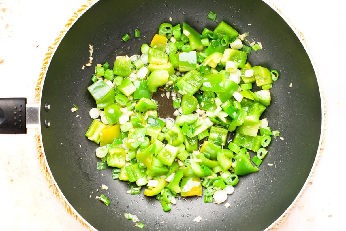 Stir frying ginger, garlic, green peppers and spring onions in a wok.