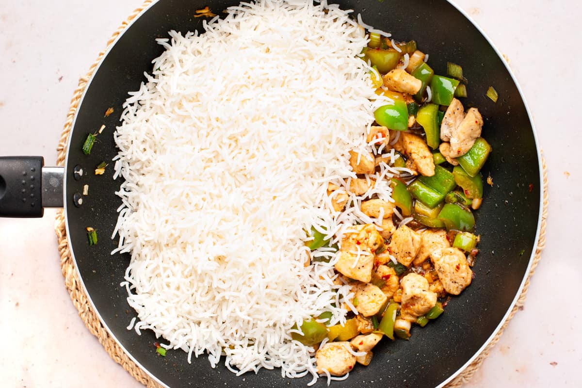 Chicken and vegetables in sauce with cooked white rice on top in a wok.